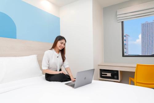 a woman sitting on a bed with a laptop at Hop Inn Hotel Iloilo in Iloilo City