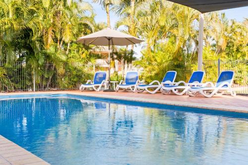 a group of blue chairs and an umbrella next to a swimming pool at Arlia Sands Apartments in Hervey Bay
