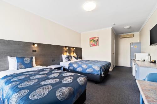 a hotel room with two beds and a desk at Colac Central Motel in Colac