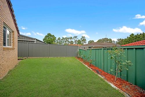 a backyard with a fence and a yard with grass at Discover Mount Annan Spacious 6-BR House in Narellan