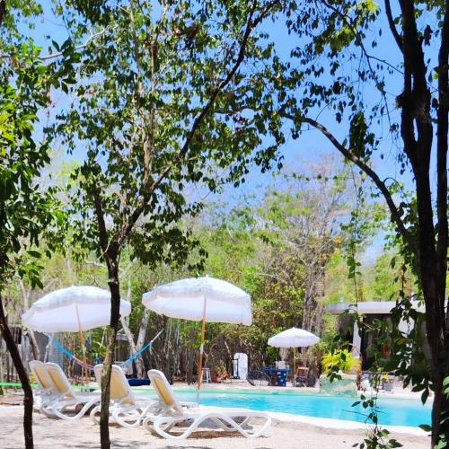 two white umbrellas and chairs next to a swimming pool at Menhir Maya in Xetna