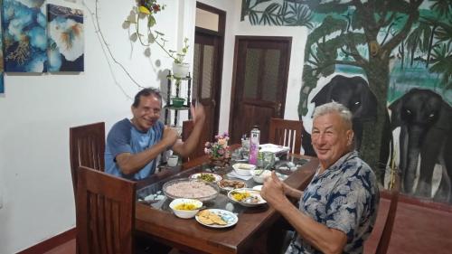 Dois homens sentados numa mesa com comida. em Tamarind Ceylon Residence em Ambalantota