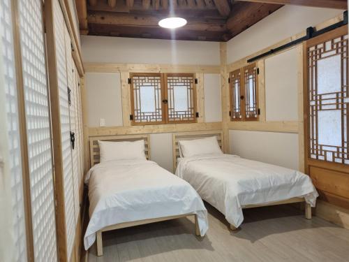 two beds in a small room with windows at Naru Hanok stay in Jeonju