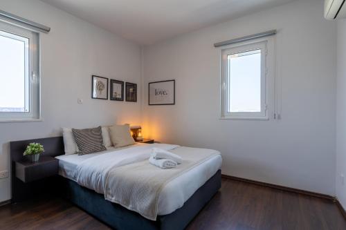 a white bedroom with a large bed and two windows at Harbor Apartments in Larnaca in Larnaka