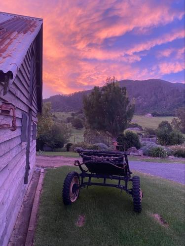 a wagon sitting outside of a barn with a sunset at Mountain View Tilba Tilba - Glamping in Tilba Tilba