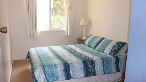 a bedroom with a bed with a blue blanket and a window at Winda Woppa Magic in Hawks Nest