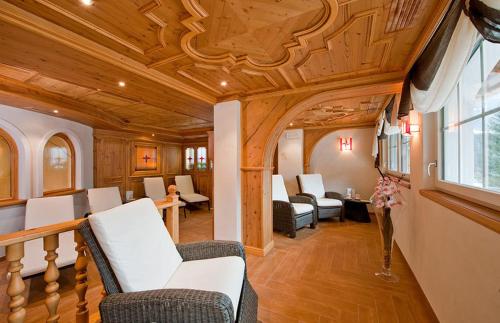 a living room with white furniture and a wooden ceiling at Hotel Des Alpes in Soraga