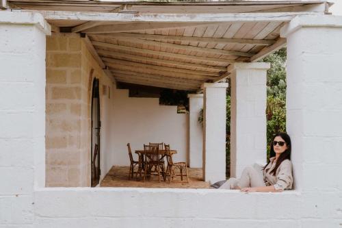 a woman sitting on the porch of a house at Masseria della Piana in Villanova di Ostuni