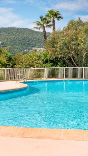 une piscine bleue avec une clôture blanche et des palmiers dans l'établissement L'AMARRE, Magnifique vue - hauteurs de Cavalaire, à Cavalaire-sur-Mer