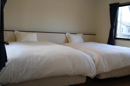 two white beds in a bedroom with a window at 一棟貸しnuevoL8～丁度良い田舎、沼田で暮らすように泊まろう in Numata