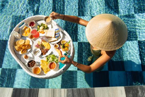 a person in a straw hat holding a tray of food by a pool at GRAND OCEAN BAY RESORT PHU QUOC in Phu Quoc