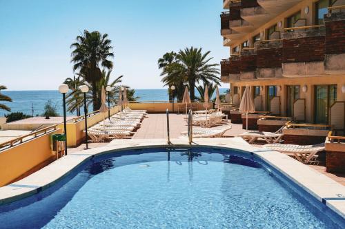 una piscina junto a un edificio con sillas y el océano en htop Royal Sun #htopFun, en Santa Susanna