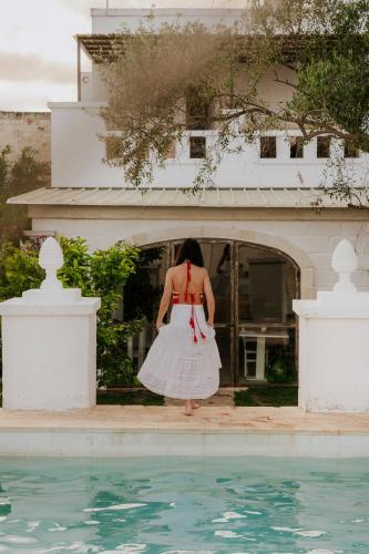 a woman in a white dress standing next to a swimming pool at Masseria della Piana in Villanova di Ostuni