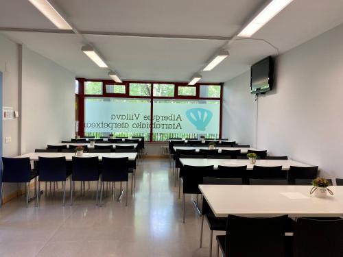 una sala de conferencias con mesas, sillas y una pantalla en Albergue de Villava en Villava