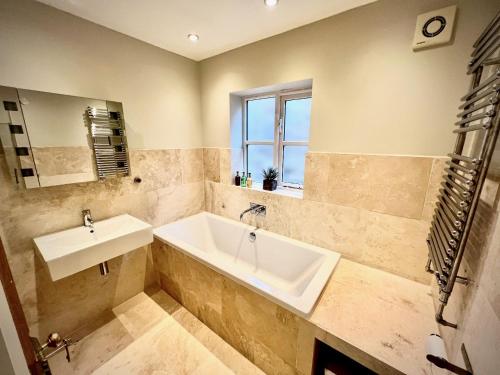 een badkamer met een bad, een wastafel en een raam bij Honey Hill Cottage - 4 Bedroom Detached House in Cambridge
