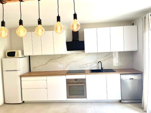 a kitchen with white cabinets and lights hanging from the ceiling at Mini maison entre mer et montagne in Aléria