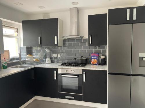 een keuken met zwarte kasten en een roestvrijstalen koelkast bij Feltham rest place in Feltham