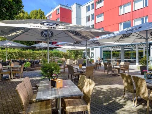 un patio al aire libre con mesas, sillas y sombrillas en Mercure Hotel Köln West en Colonia