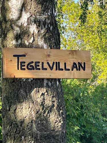 a wooden sign hanging on a tree at Tegelvillan på golfbanan in Oxie