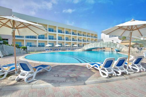 a pool with chairs and umbrellas next to a hotel at Radisson Blu Resort, Fujairah in Dibba
