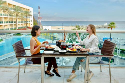 two women sitting at a table eating food on a balcony at Radisson Blu Resort, Fujairah in Dibba