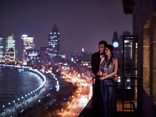 un homme et une femme debout sur un balcon la nuit dans l'établissement Fairmont Peace Hotel On the Bund, à Shanghai