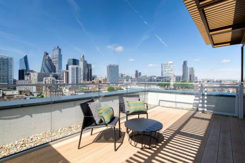 einen Balkon mit 2 Stühlen, einem Tisch und einer Skyline der Stadt in der Unterkunft Hyatt Place London City East in London