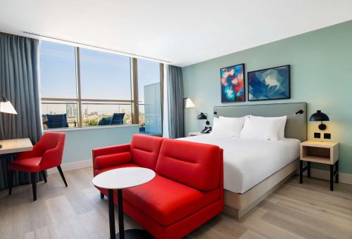 um quarto de hotel com uma cama e uma cadeira vermelha em Hyatt Place London City East em Londres