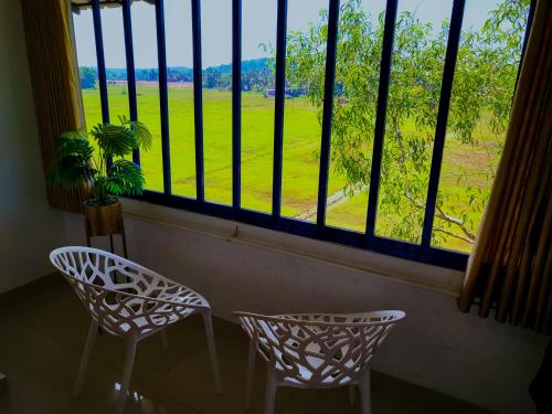 two chairs and a window with a view of a field at Thejaswini Residency Cheruvathur in Nīleshwar