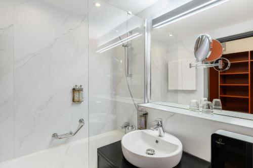 a white bathroom with a sink and a shower at Danubius Hotel Hungaria City Center in Budapest