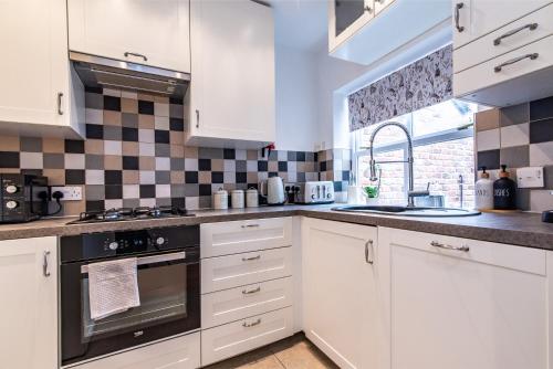 uma cozinha com armários brancos e electrodomésticos pretos em Blackfriars House, overlooking Chester Racecourse em Chester