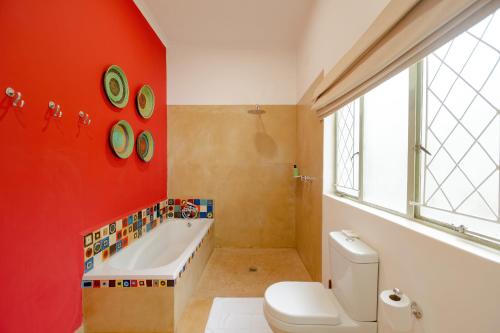 baño con pared roja, bañera y aseo en PheZulu Guest Lodge en Victoria Falls