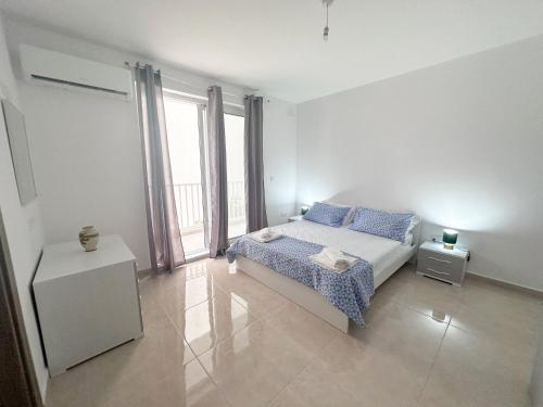 a white bedroom with a bed and a large window at AP Central Swieqi in Is-Swieqi