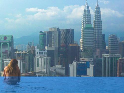 a woman sitting in a infinity pool looking at a city at Harmony Luxury Suites At Lucentia Bukit Bintang City Center in Kuala Lumpur