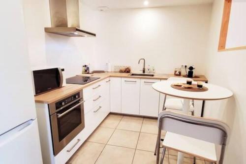 une cuisine avec des armoires blanches, une table et un micro-ondes dans l'établissement Appartement Duplex 3 chambres - La Blache des Collines, à Beausemblant