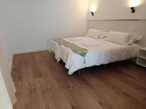 a bedroom with a bed with white sheets and wooden floors at SG ROOMS in Consuegra