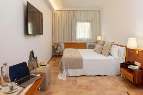 a bedroom with a bed and a desk with a laptop at Hotel Spa Porto Cristo in Port de la Selva