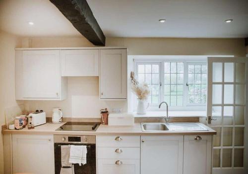 una cocina con armarios blancos y fregadero en Aynho Cottages, en Banbury