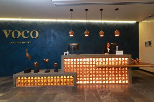 a woman is sitting at a desk in a lobby at voco Guadalajara Neruda by IHG in Guadalajara