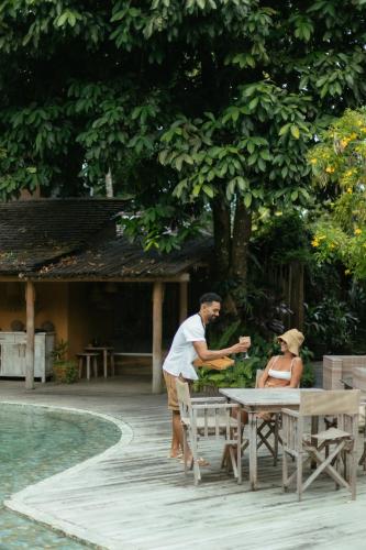 a man and woman sitting at a table near a pool at Pousada Capim Santo in Trancoso