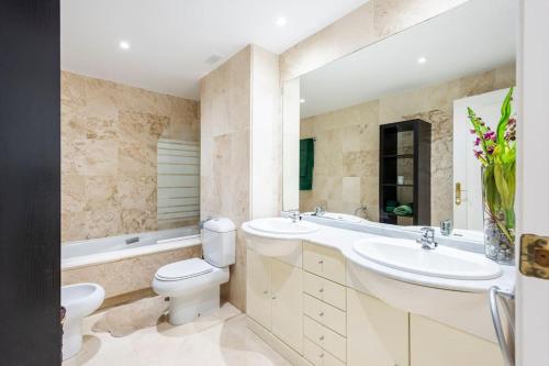 Un baño con dos lavabos, un inodoro y una bañera. en Apartamento en Marbella Guadalmina primera linea de campo de golf Los Cartujanos, en Marbella
