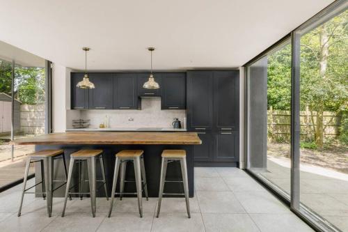 a kitchen with black cabinets and bar stools at Parea Living - Spacious North London House with Big Garden in London
