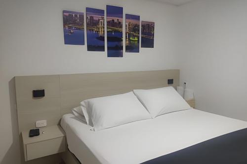 a white bed in a room with paintings on the wall at Amplios Apartamentos San Fernando Cerca a Centros Médicos in Cali
