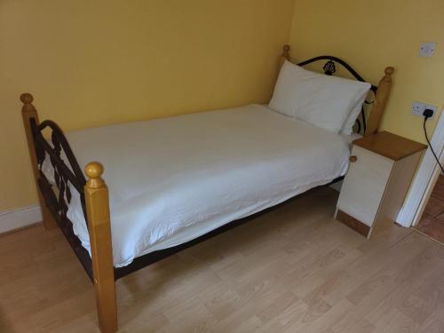 a bed with a wooden frame and white sheets and a night stand at Sheraton Lodge Apartments t12e309 in Cork