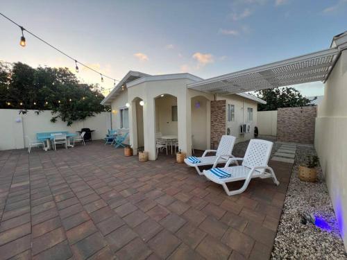 a patio with white chairs and tables on it at Cozy House Aruba in Palm-Eagle Beach