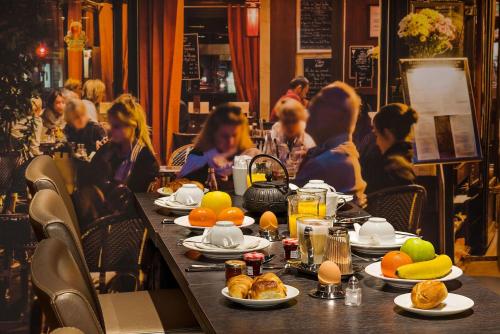 a table with plates of food and people in a restaurant at Midnight Hôtel Paris in Paris