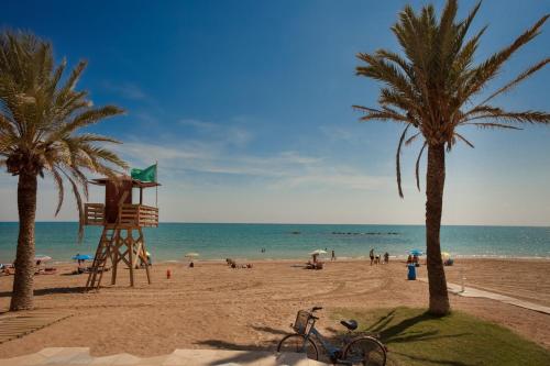 a beach with a life guard tower and palm trees at Hotel RH Vinaros Playa & Spa 4* Sup in Vinaròs
