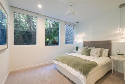 a white bedroom with a bed and two windows at Azure in Sunshine Beach