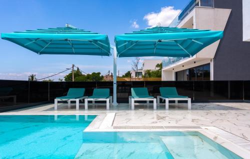 a group of blue chairs and umbrellas next to a swimming pool at Gorgeous Home In Crikvenica With Sauna in Crikvenica
