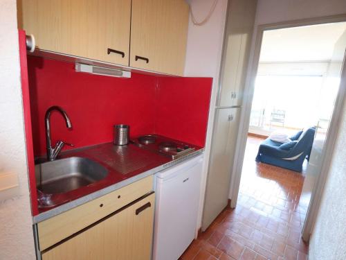 - une cuisine avec un évier et un mur rouge dans l'établissement Studio avec piscine, parking et terrasse à Port Camargue - FR-1-307-262, au Grau-du-Roi